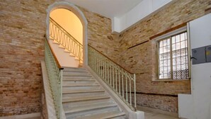 A staircase with a wooden handrail and a red carpet at the bottom, leading to a landing with a white door and a window with metal bars.