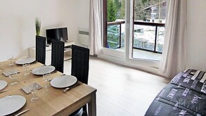 A modern living room with a wooden dining table set for four, a black sofa, and a large window with a view of a snowy landscape. - La Borgia A, B, C by Interhome (Les Contamines)