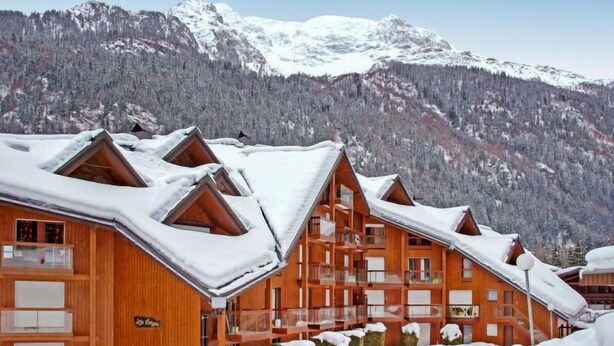 A wooden chalet-style building with multiple balconies, surrounded by snow-covered mountains. - La Borgia A, B, C by Interhome (Les Contamines)