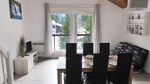 A modern living room with a dining table, chairs, a sofa, a TV, and a large window with curtains. - La Borgia A, B, C by Interhome (Les Contamines)