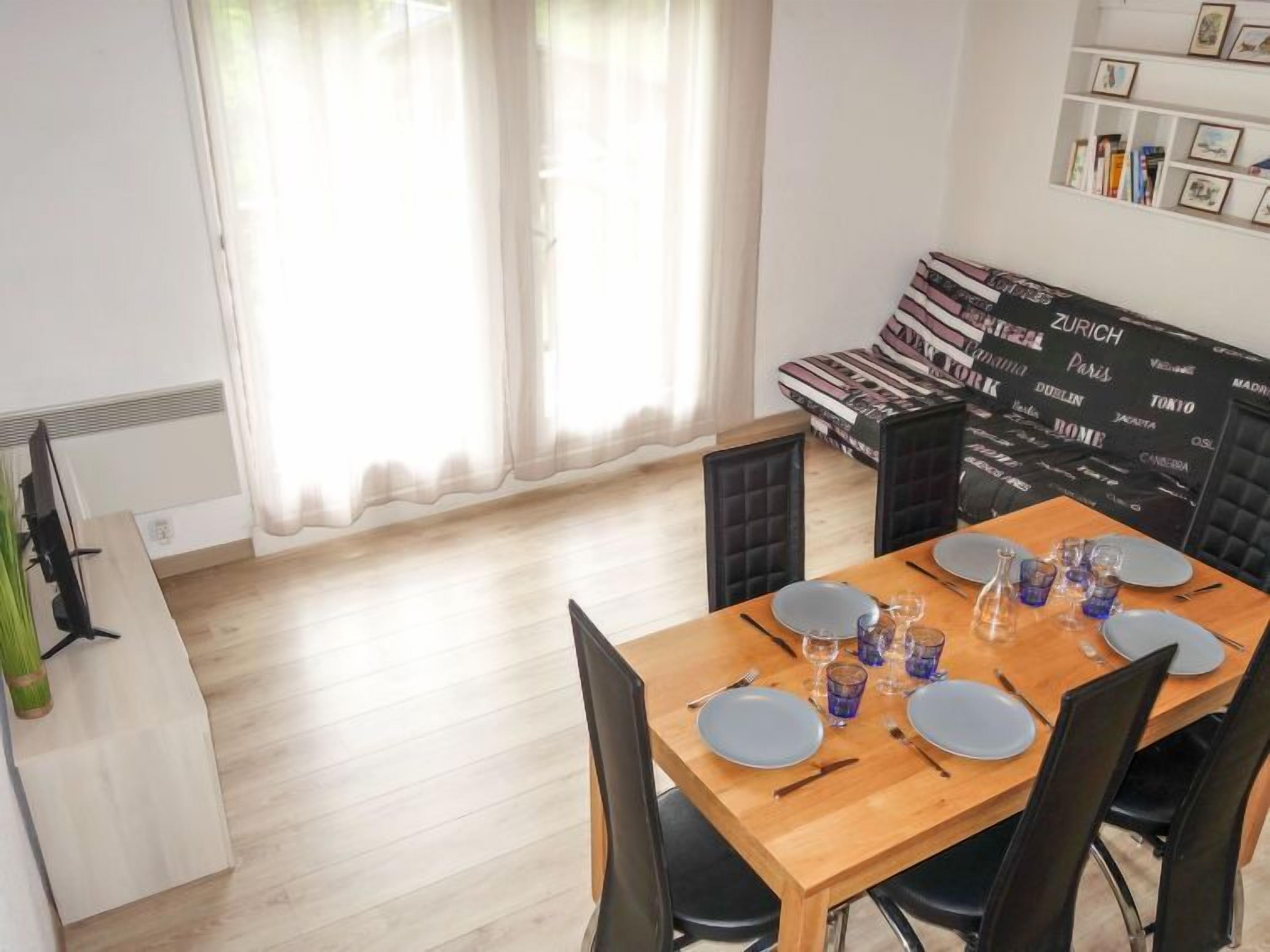 Un coin repas avec une table en bois dressée pour quatre personnes, des chaises noires et un canapé noir rembourré placé contre un mur orné de tableaux.