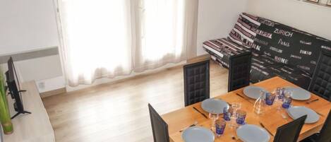 Un coin repas avec une table en bois dressée pour quatre personnes, des chaises noires et un canapé noir rembourré placé contre un mur orné de tableaux.