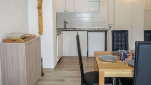 A compact kitchen with white cabinets, a small sink, and a dishwasher. There is a dining table with chairs and a set of plates and glasses. - La Borgia A, B, C by Interhome (Les Contamines)