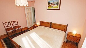 A bedroom with a large bed, two bedside tables with lamps, a wooden chair, a door, and a framed picture on the wall. - La Busa by Interhome (Alleghe)