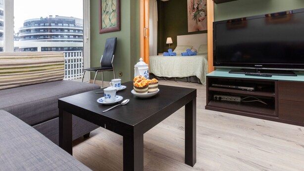 A modern living room with a sofa, a coffee table, a TV, and a dining area with a table set for two.