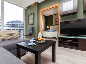 Una sala de estar moderna con un sofá, una mesa de centro, un televisor y un comedor con una mesa preparada para dos.