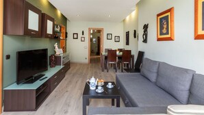 A modern living room with a flat-screen TV, a sofa, a dining area with chairs, and a coffee table.