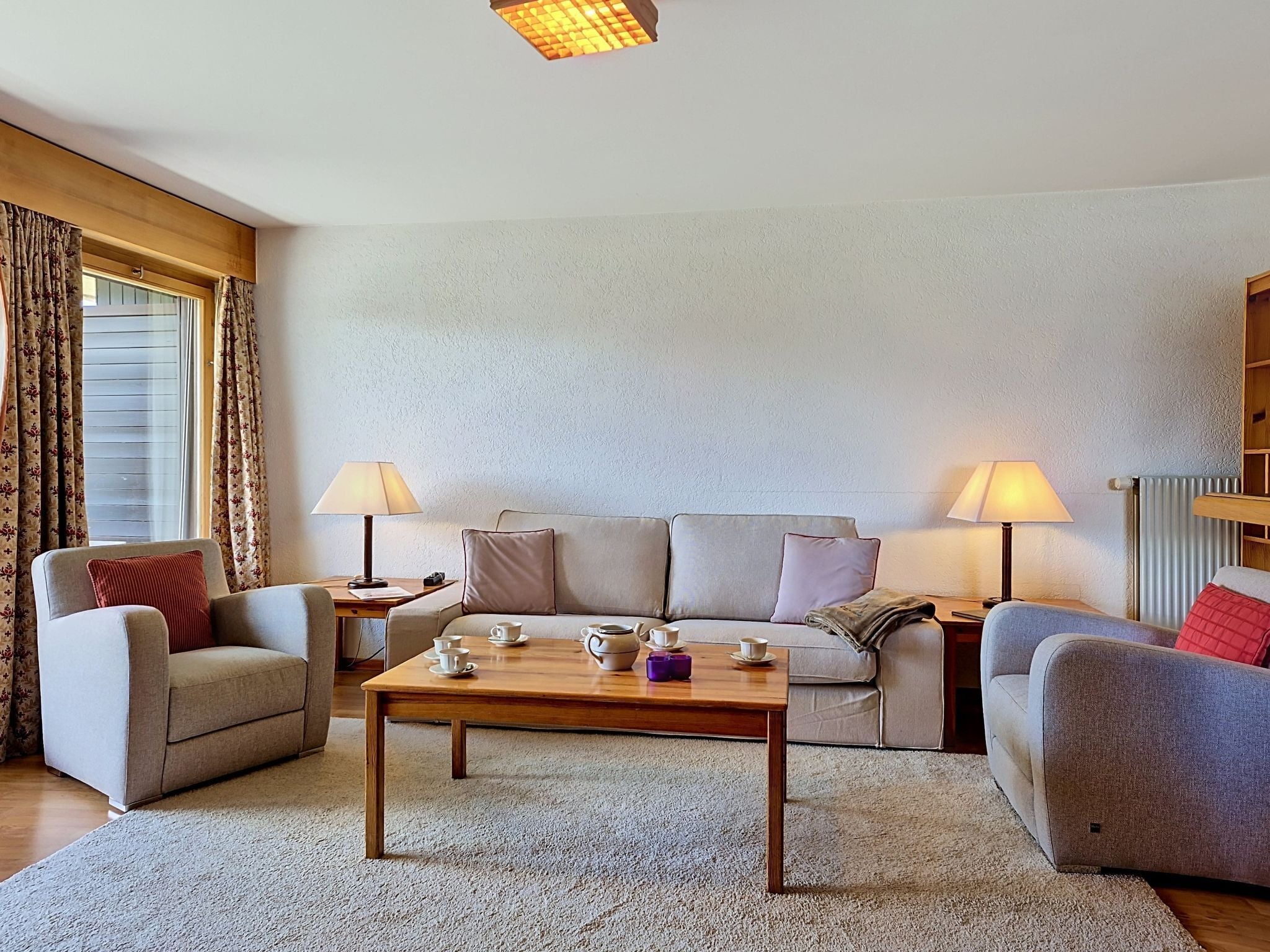 Un salon comprenant un canapé, deux fauteuils, une table basse, des lampes et une fenêtre avec des rideaux.