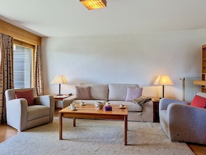 A living room with a sofa, two armchairs, a coffee table, lamps, and a window with curtains.