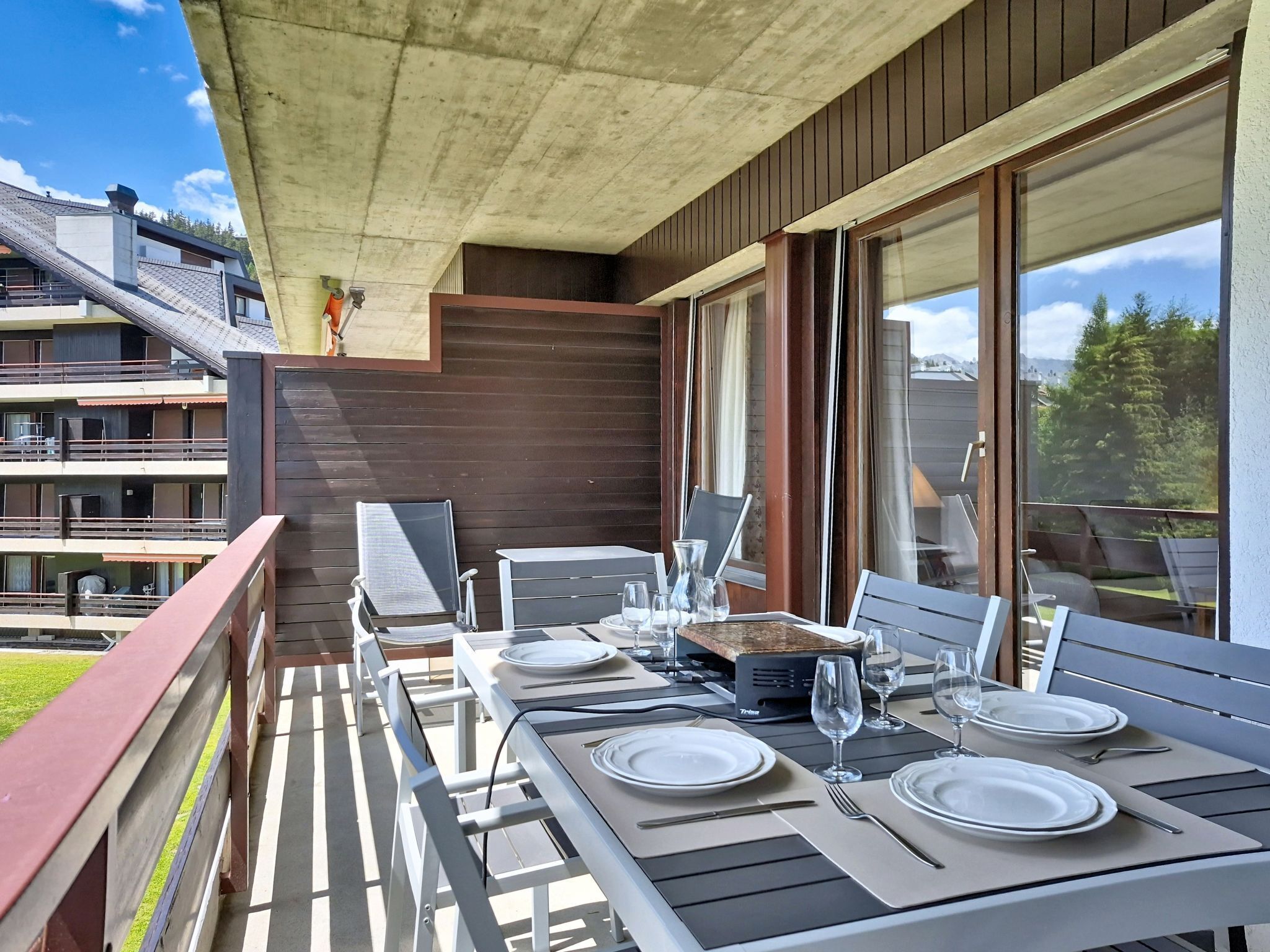 Un balcón con una mesa lista para comer, sillas y vista a un edificio con varios balcones.