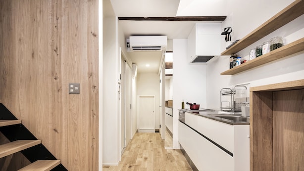 A narrow hallway with wooden flooring and a kitchen area on the right, featuring white cabinets and wooden shelves. - Japan Sessions KANZAKI 01 (Osaka)