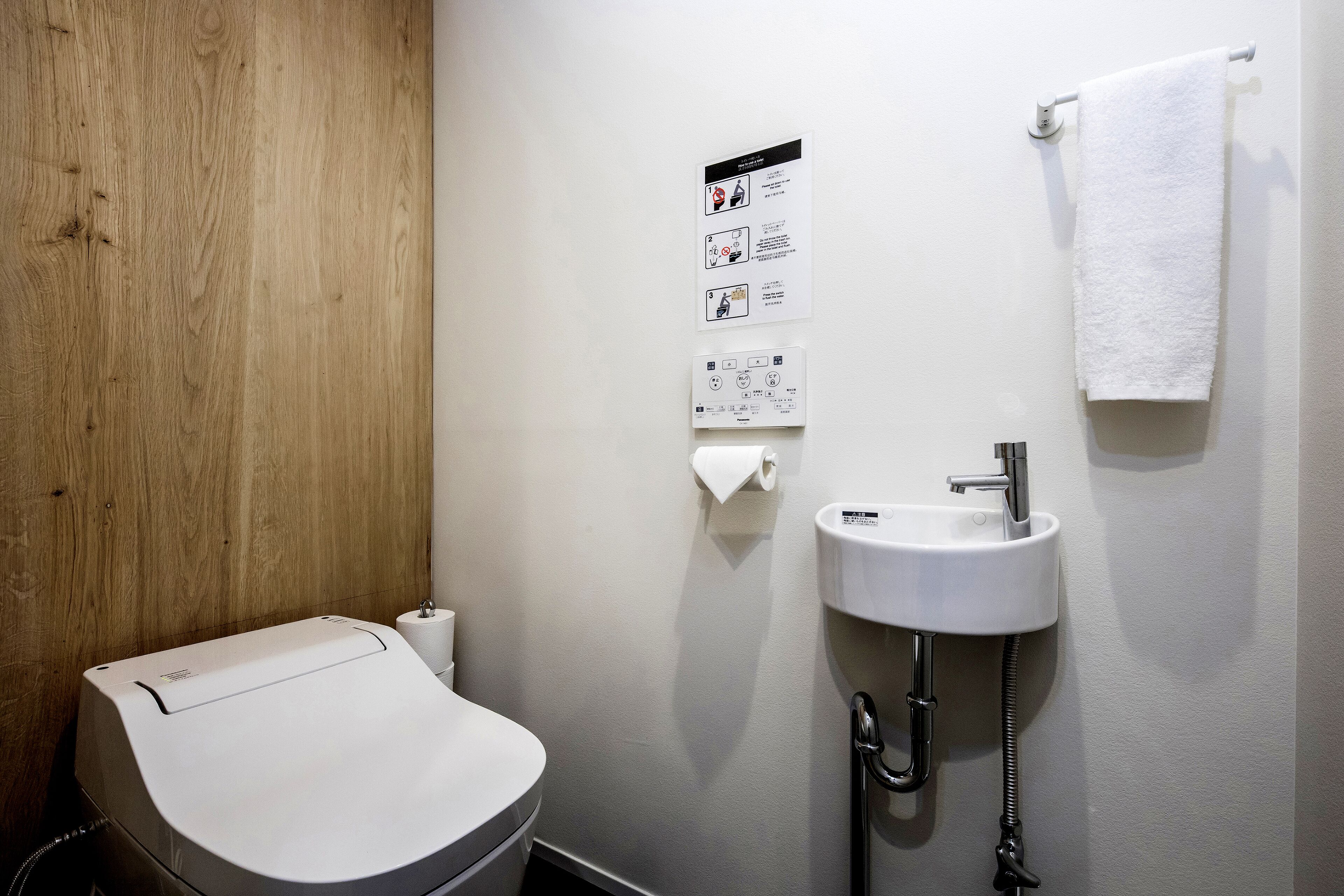 A small, modern bathroom with a toilet, sink, and towel hanging on the wall.
