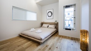 A modern bedroom with a wooden bed, a window with a view, and a wall-mounted air conditioner. - Japan Sessions KANZAKI 01 (Osaka)