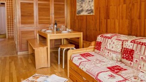 A cozy room with wooden walls, a dining table set with plates and glasses, a sofa with a patterned cover, and a painting on the wall. - Les Moutières B1 et B2 (Val Claret) by Interhome (Tignes)