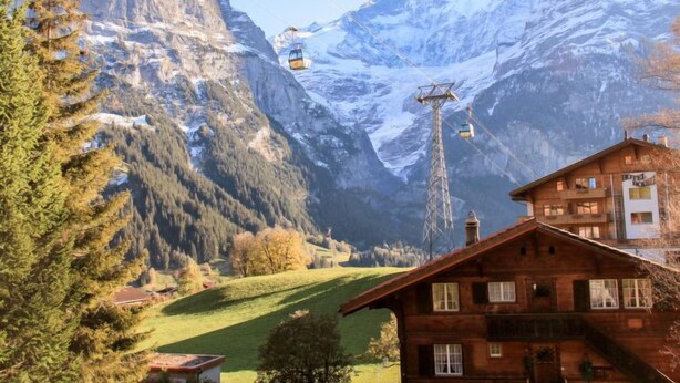 Et fjeldhotel med træfacade, skilift i baggrunden og snedækkede bjerge.
