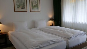 En dobbeltseng med hvide sengetøj, to vægmonterede lamper og to indrammede landskabsmalerier.