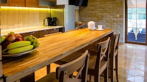 Een moderne keuken met houten kasten, een stenen muur, een houten eettafel en een aan de muur bevestigde televisie.