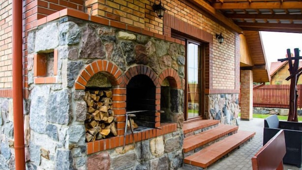 Een gebouw van steen met twee bakovens, een houten bank en een overdekt terras.