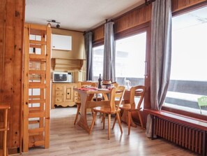 A cozy room with a wooden dining table, chairs, a small kitchen area with a microwave, and a window with curtains.