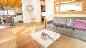 A spacious living area with a wooden ceiling, a sofa with decorative pillows, a coffee table with a vase, and a kitchen in the background. - Apartment Lanner by Interhome (Axams)