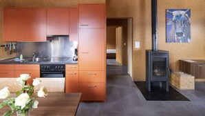 A modern kitchen with orange cabinets, a stove, and a sink. There is a wooden table with a vase of white flowers. A painting of a cow is on the wall.