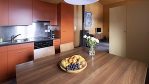 A modern kitchen with orange cabinets, a wooden dining table with a fruit bowl, and a white pendant light.