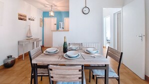 Un coin repas avec une table en bois dressée pour quatre personnes, des chaises, une horloge et une porte sur la droite.