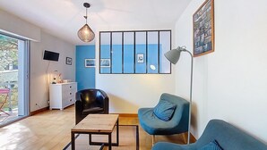 Un salon moderne avec un canapé bleu, un fauteuil noir, une table basse en bois, un lampadaire et une grande fenêtre donnant sur un paysage verdoyant.