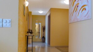 A hallway with yellow walls, a tiled floor, and a painting on the right. There is a small table with a vase and a mirror on the left. - Viktoria B by Interhome (Zermatt)