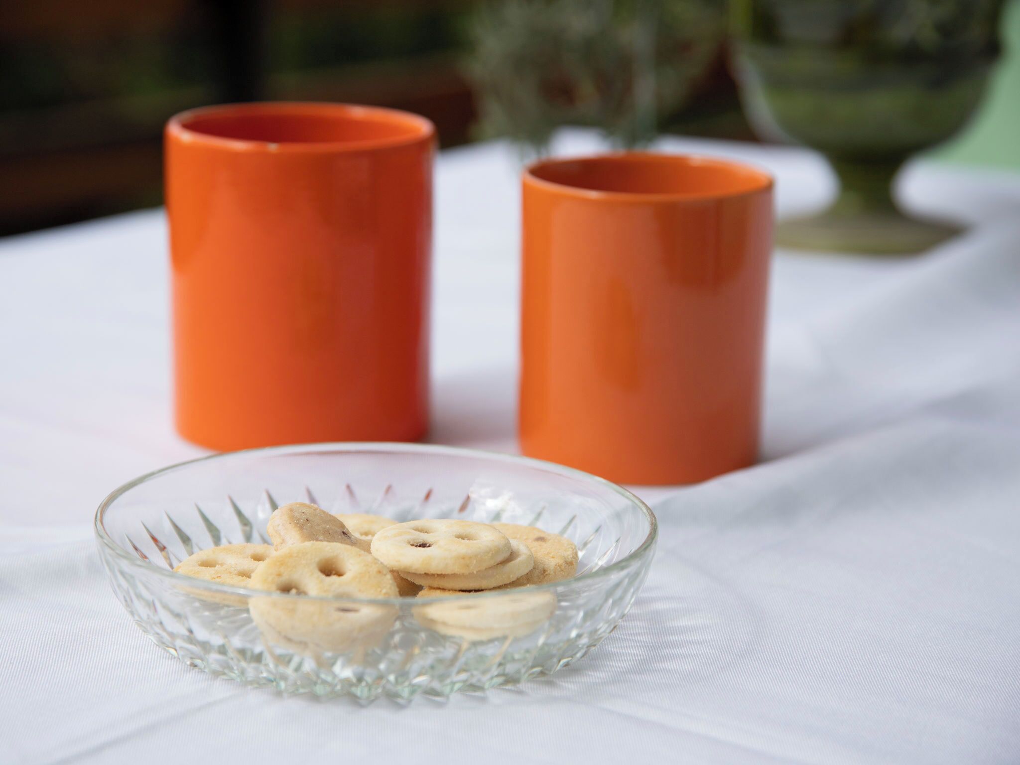 A clear glass bowl with cookies on a white tablecloth.