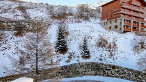 A stone bridge over a snow-covered landscape with a building featuring balconies in the background. - Armoise 51 by Interhome (Les Menuires)