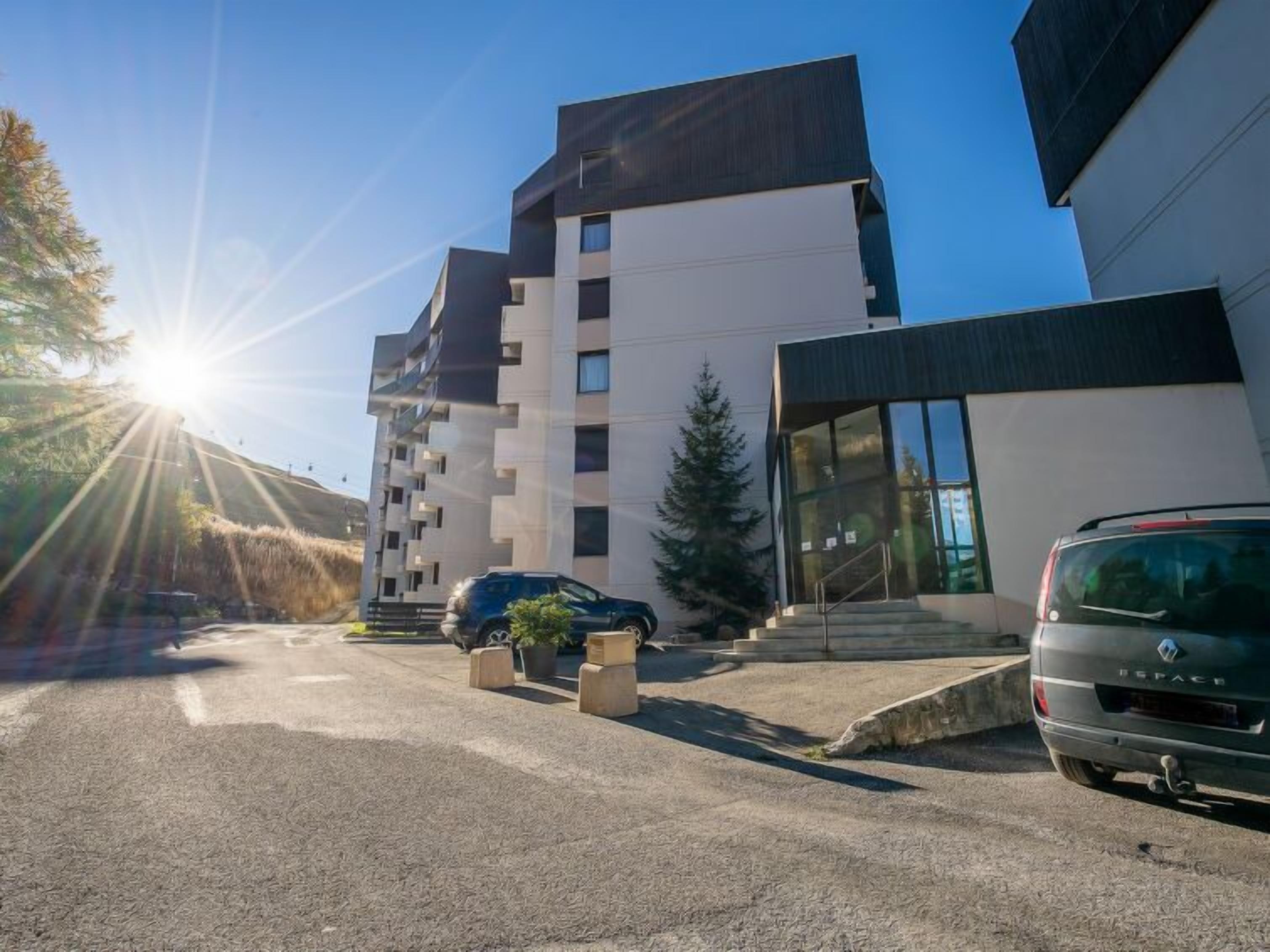 En moderne bygning med parkeringsplads, en parkeret bil og en klar himmel.
