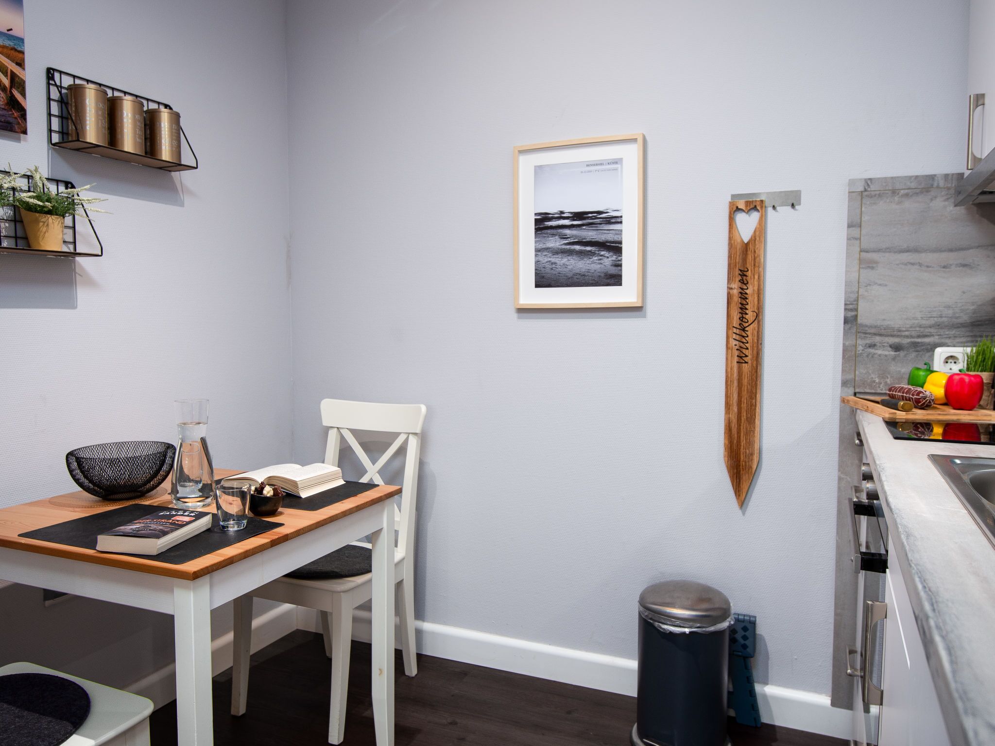 Una cocina moderna con una silla blanca, una mesa de madera, una fotografía enmarcada y un letrero de madera colgante.