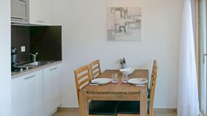 Ett kompakt kök med en matplats, inklusive ett träbord med fyra stolar, en tavla på väggen och utsikt över omgivningen.