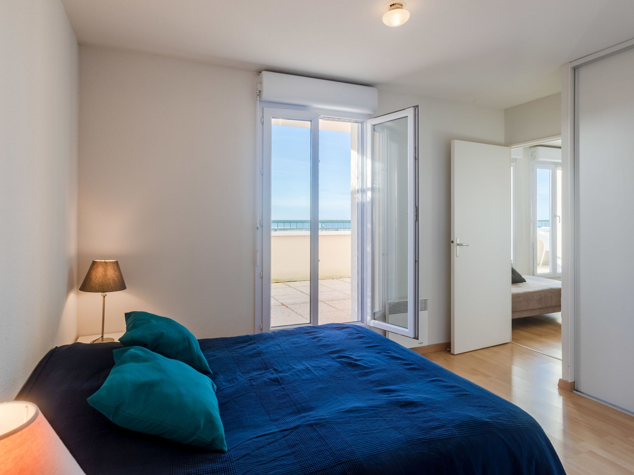Una camera da letto con un letto, una lampada e vista sulla spiaggia attraverso una porta aperta.