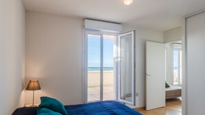 Une chambre avec un lit, une lampe et une vue sur la plage, visible par une porte ouverte.