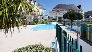 Une piscine entourée d’une clôture verte, avec des bâtiments en arrière-plan.