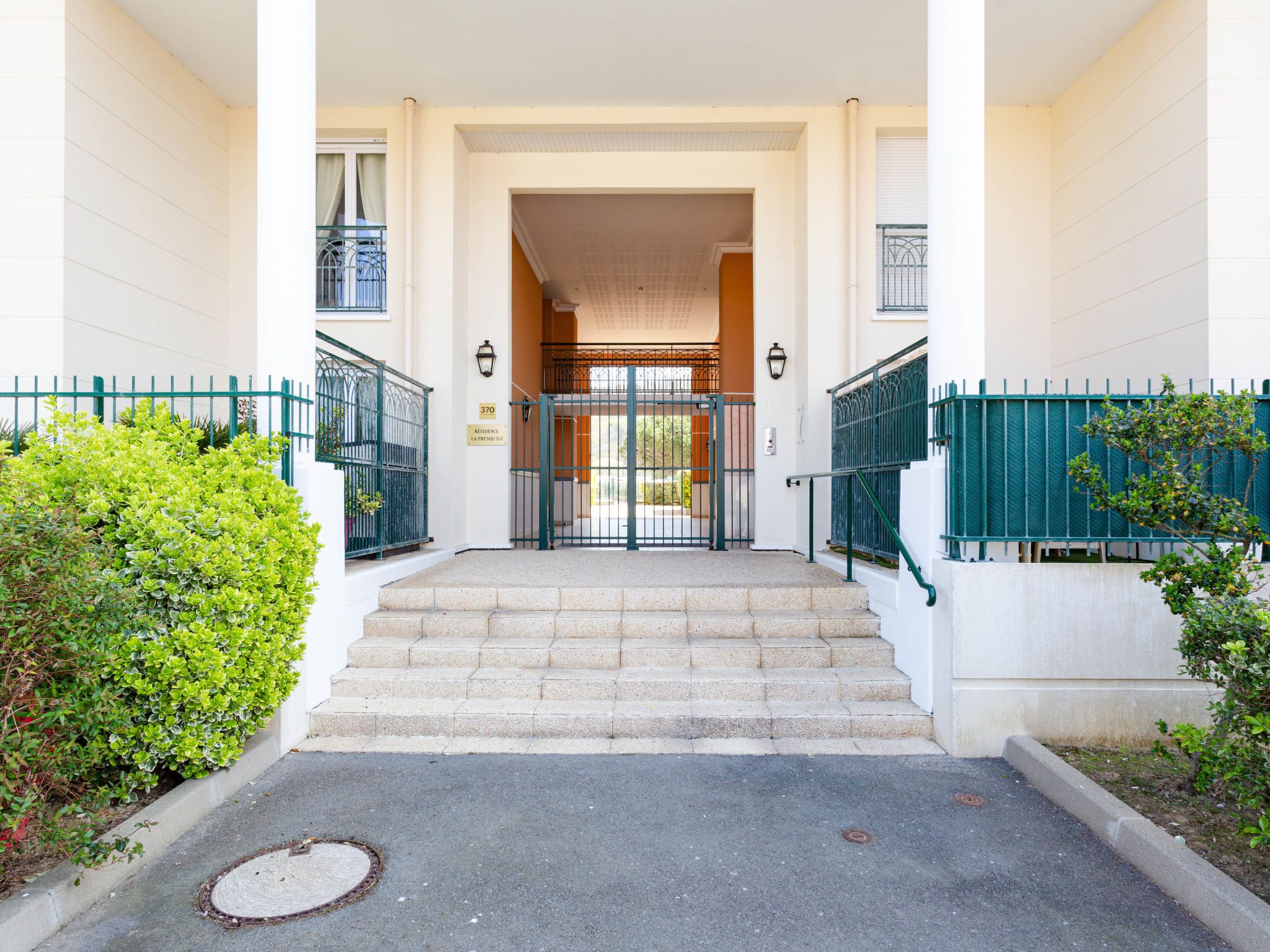 A building entrance with a gated driveway, steps leading to a door, and a small garden area.