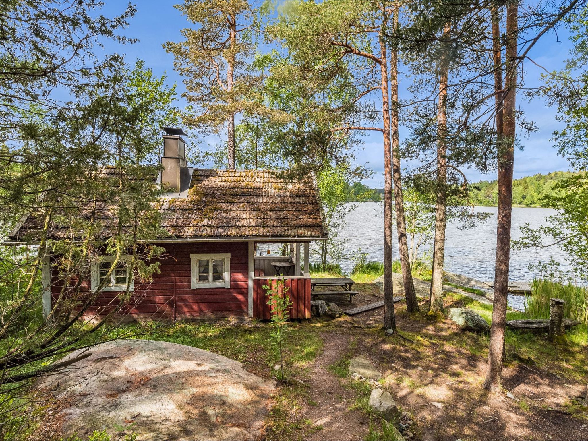 En hyggelig hytte med skorsten, terrasse og udsigt over en sø.