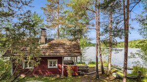 A rustic cabin with a chimney, surrounded by trees and a lake.