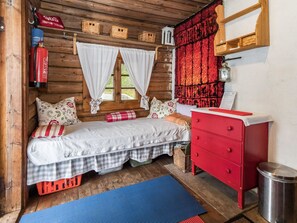A cozy cabin room with a bed, a red dresser, a small window with curtains, and a fire extinguisher.