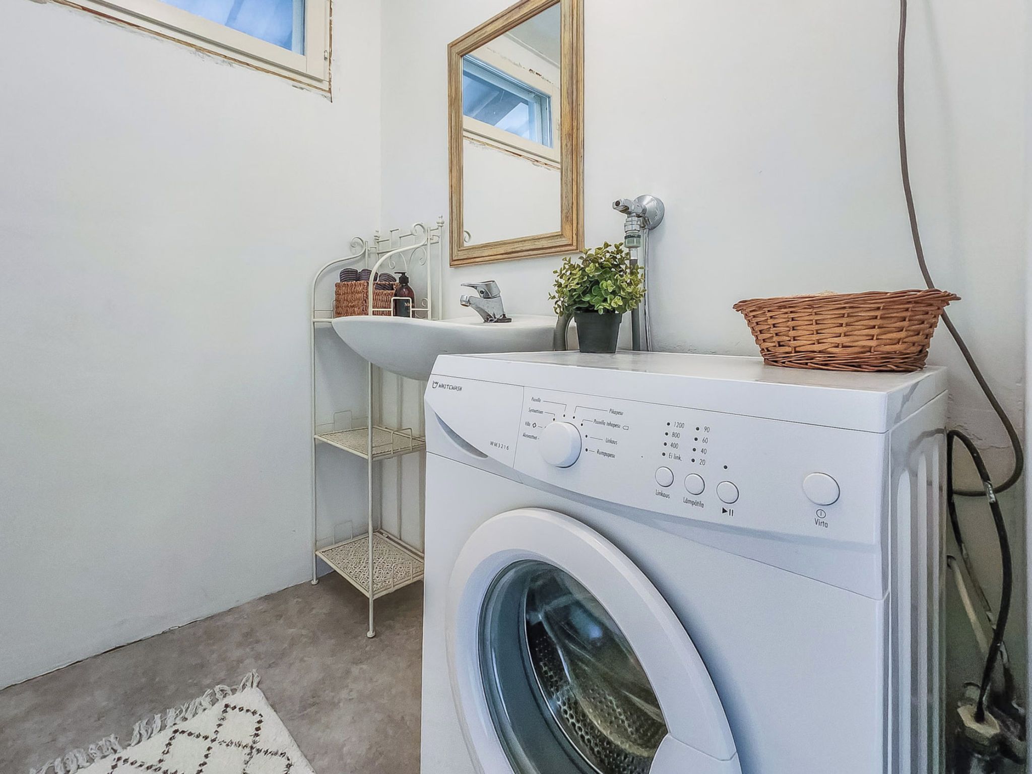 A compact laundry area with a washing machine, a sink, and a mirror.