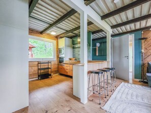 A modern kitchen with wooden cabinets, a bar area with stools, and a large window overlooking greenery.