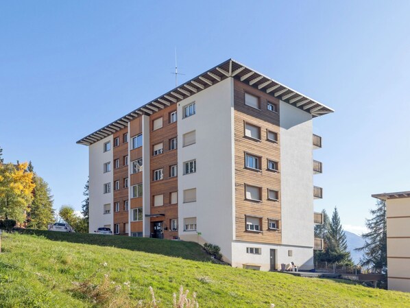 A multi-story residential building with a flat roof, large windows, and a balcony on the upper floor.