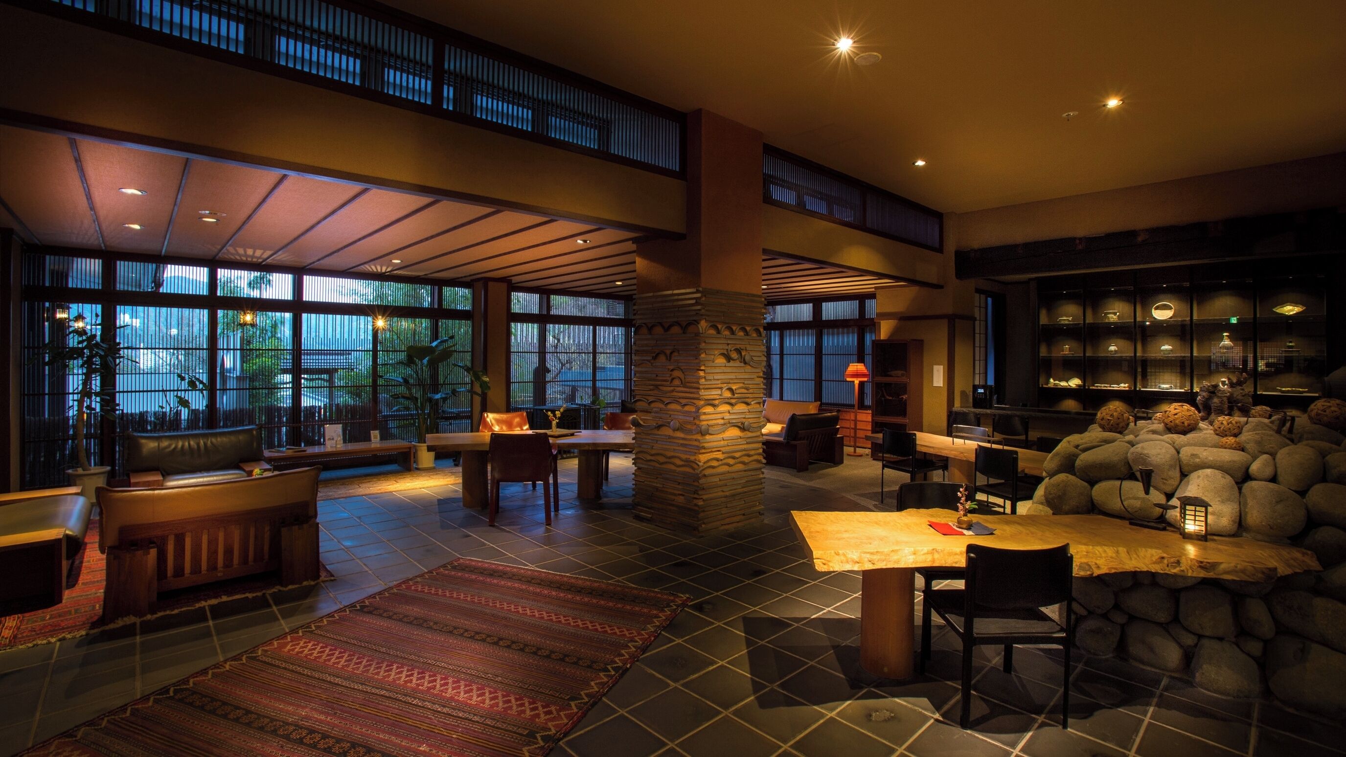 A spacious interior with a high ceiling, large windows, a stone pillar, and a dining area.