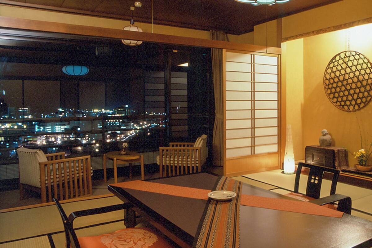 Ein traditioneller japanischer Raum mit Tatami-Böden, einem niedrigen Tisch und Blick auf eine nächtliche Stadtansicht.