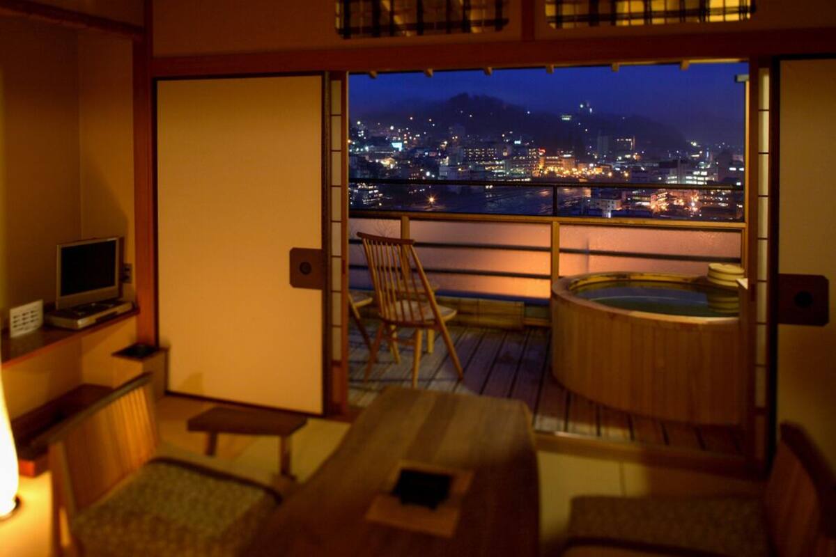 Ein Zimmer mit Blick auf die Stadt, einer Badewanne, einem Fernseher und einer traditionellen japanischen Schiebetür.