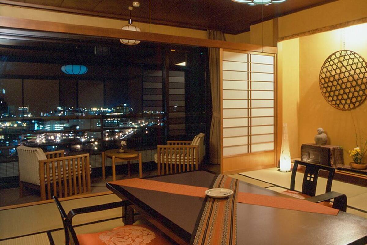 Ein traditioneller japanischer Raum mit Tatami-Böden, einem niedrigen Tisch und Blick auf die nächtliche Stadt.