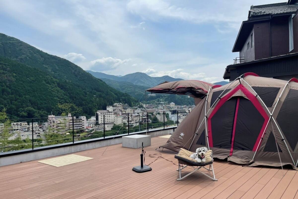 Eine Dachterrasse mit Zelt und Hundebett, mit Blick auf Stadt und Berge.