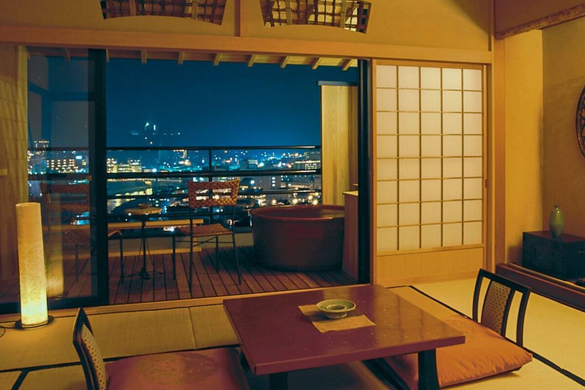 Ein Zimmer mit Blick auf eine nächtliche Skyline, einer Schiebetür, einem Tisch mit Kissen und einem dekorativen Gegenstand an der Wand.